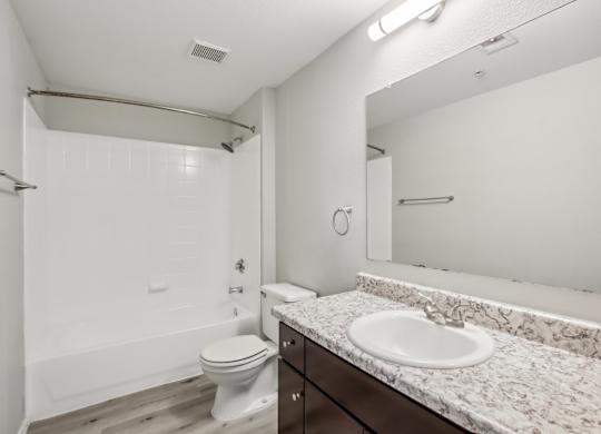 A white bathroom with a toilet, sink, and mirror at Sweetwater At Metro North Apartments, Phoenix, Arizona
