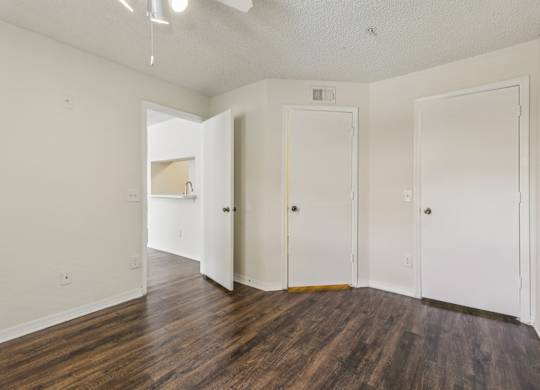 A room with white walls and wood flooring with three doors.