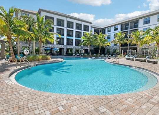 A large swimming pool surrounded by palm trees and a building in the background.