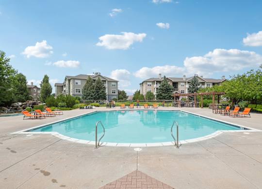 A swimming pool surrounded by orange chairs and trees.