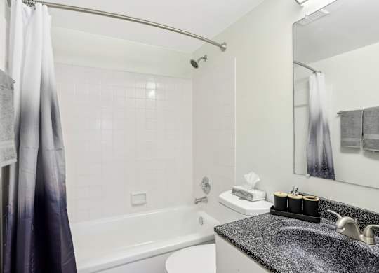 A bathroom with a white tub, sink, and grey tiles. at Millennium at Creve Coeur, Creve Coeur, 63141