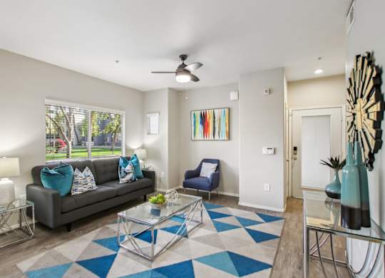 A living room with a grey couch, a blue chair, and a glass coffee table at Sweetwater At Metro North Apartments, Phoenix, AZ