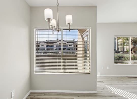 A room with a large window covered by white blinds and a chandelier hanging from the ceiling at Sweetwater At Metro North Apartments, Phoenix