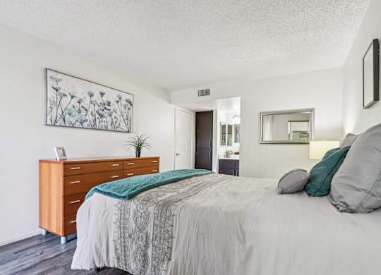 A bedroom with a bed, nightstand, and a plant.
