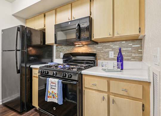 A kitchen with a black refrigerator and stove top oven.