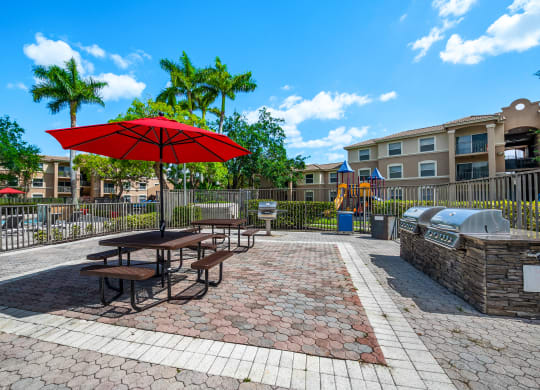 a picnic area with picnic tables and an umbrella in front of an apartment building at Pembroke Pines Landings, Pembroke Pines, FL, 33025