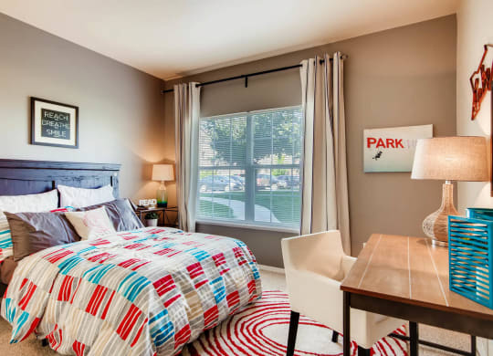 a bedroom with a bed and a desk with a window at Heritage at Stone Mountain, Northglenn, CO, 80233