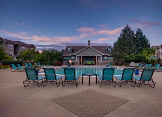 a pool with blue chairs around it and a house in the background at Heritage at Stone Mountain, Northglenn, CO, 80233