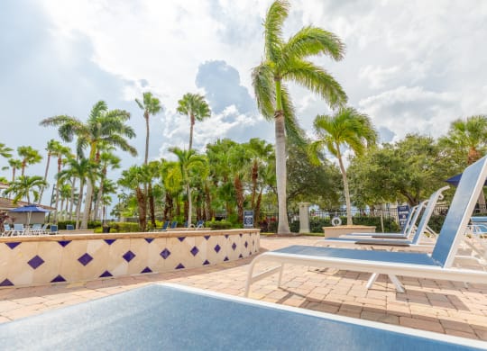 a resort style pool with chaise lounge chairs and palm trees in the background at Heritage Bay, Jensen Beach, 34957