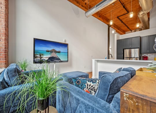 a living room with couches and a kitchen with a tv on the wall at Riverwalk Apartments, Lawrence, MA
