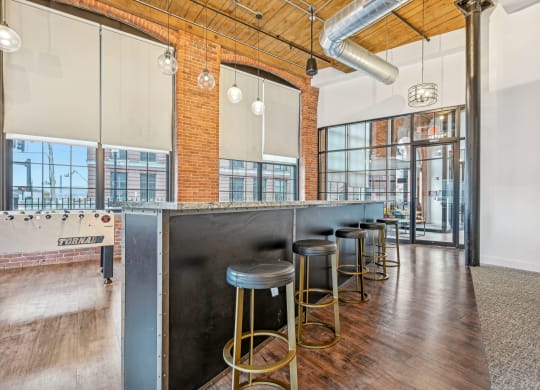 a long bar with stools and a exposed brick wall and glass doors at Riverwalk Apartments, Lawrence, MA