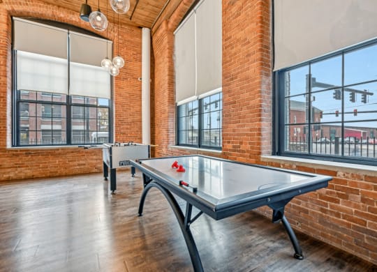 two ping pong tables in an empty game room with brick walls and large windows at Riverwalk Apartments, Lawrence, MA