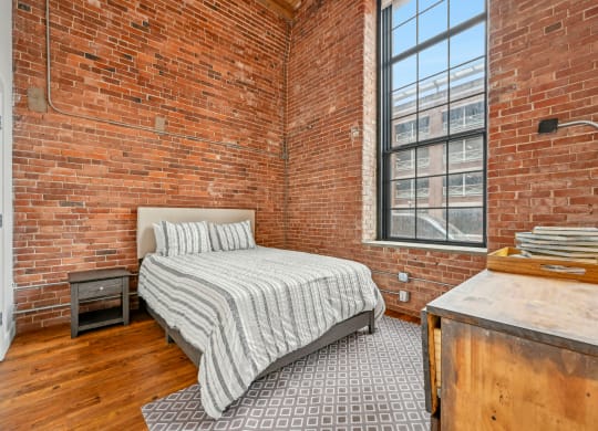 a bedroom with a bed and a brick wall at Riverwalk Apartments, Lawrence, MA