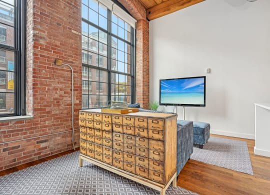 a living room with a large window and a dresser with a tv on it at Riverwalk Apartments, Lawrence, MA