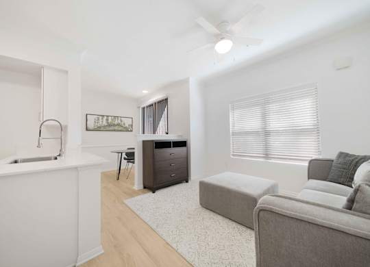 A modern living room with a grey couch and a white kitchen area.