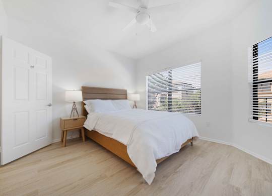 A bedroom with a bed, nightstand, and window with blinds.