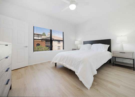 A bedroom with a bed, nightstand, and window with blinds.