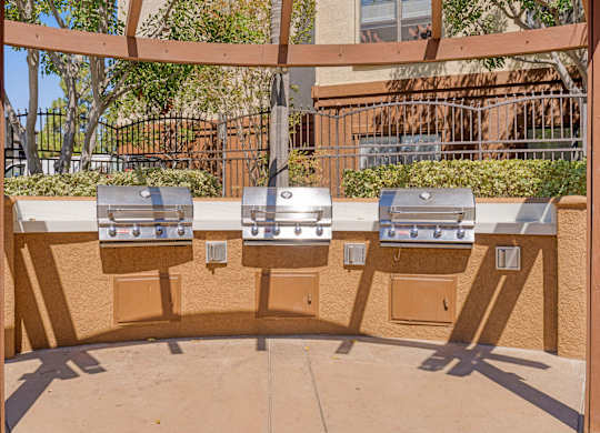 Three barbecue grills are lined up on a patio.