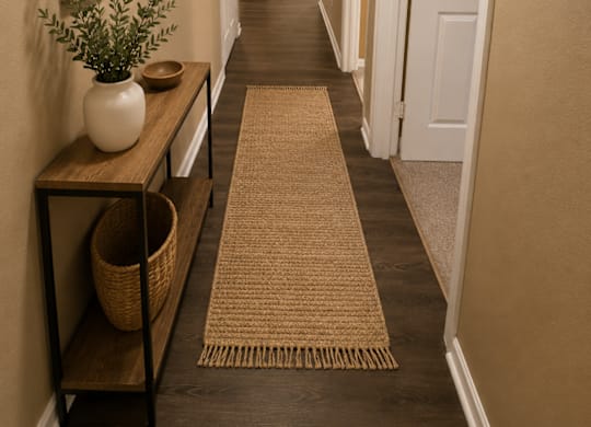 A hallway with a rug on the floor and a plant on a shelf.