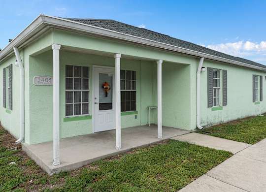a green house with white pillars and a white door at The Groves at Wimauma Apartments , Wimauma, Florida