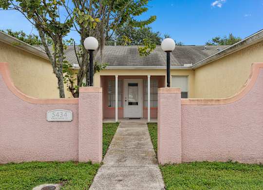the front entrance to a pink house with a sidewalk and street lamps at The Groves at Wimauma Apartments , Florida 33598
