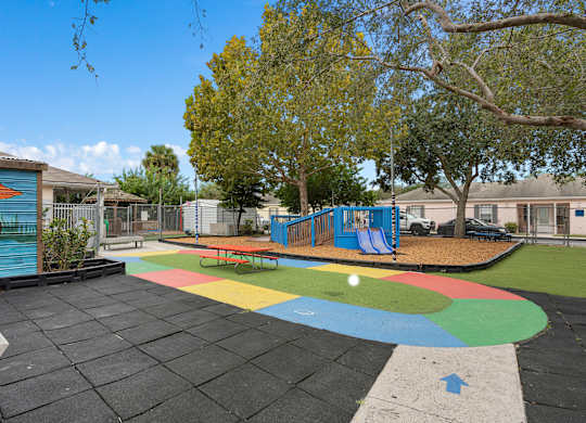 a playground with a multicolored circle in the middle of it and some trees at The Groves at Wimauma Apartments , Wimauma