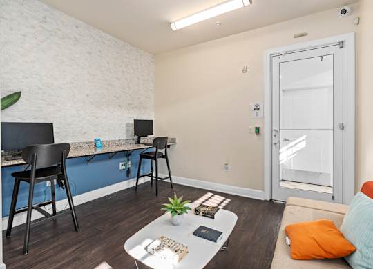 a living area with a couch and a desk with chairs and a door to a at Lake Lofts at Deerwood, Jacksonville, FL, 32216