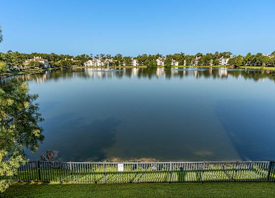a view of a lake with a fence and houses in the background at Lake Lofts at Deerwood, Jacksonville, FL, 32216
