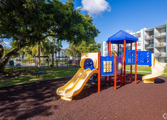 a playground with a slide and monkey bars in front of an apartment building  at Club at Emerald Waters, Hollywood, FL