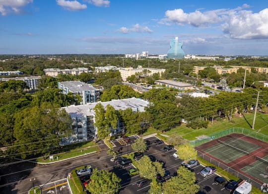 an aerial view of the campus with a tennis court in the foreground and a large building in  at Club at Emerald Waters, Florida