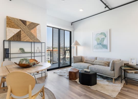 Cozy living room and dining area decorated with boho furniture and natural lighting entering from the balcony doors.