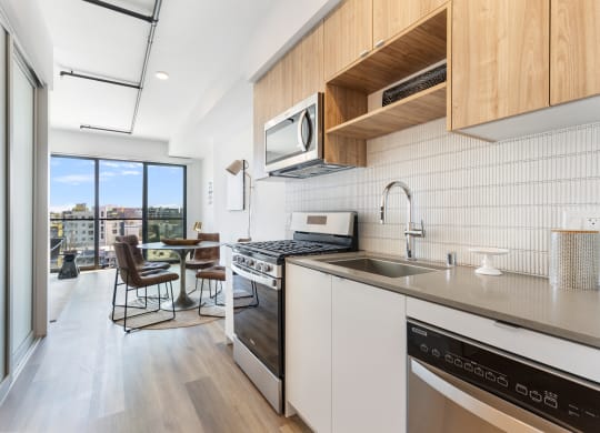 Left wing kitchen with stainless steel appliances, gray countertops, and wooden cabinetry.