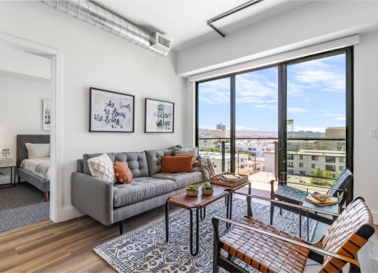 Cozy living room decorated with a gray couch, brown leather table and chairs by a beautiful outdoor balcony.