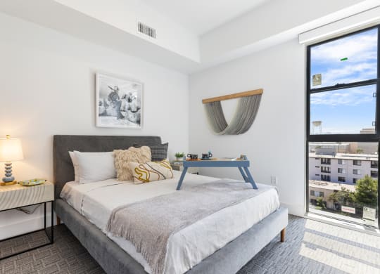 Stylish bedroom with gray queen-sized bed frame, white sheets, and gray throw complemented by an off-white nightstand.