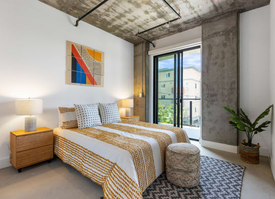 Bedroom with balcony access decorated with yellow/white bedding and colorful artwork on the wall.