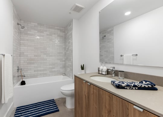 Bathroom with soaking tub, grey countertop, and wood cabinetry.