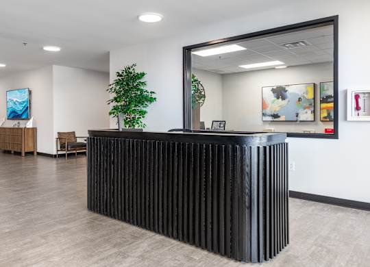 A black reception desk with a mirror above it in a room with wooden floors.