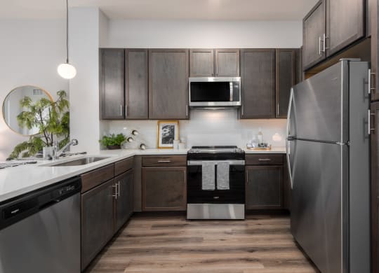 Modern kitchen with designer lighting, quartz countertops, dark cabinetry and stainless steel appliances  at Chapter at the Streets of St Charles, Saint Charles, MO
