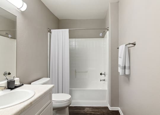 Model Bathroom with Bathtub/Shower, Wood-Style Flooring & White Cabinets at Verraso Apartments in Las Vegas, NV.