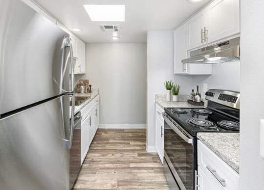 Pet-Friendly Affordable Apartments in East Tucson, AZ - Lakeside Casitas - A Kitchen With White Cabinets, Stainless Steel Appliances, Recessed Lighting, And Wood Style Flooring.