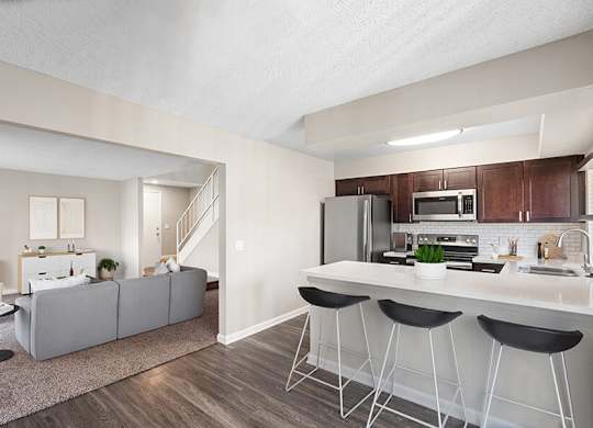 Model Kitchen with Dark Wood Cabinets, Wood-Style Flooring and View of Living Room at Horizon Apartments located in Santa Ana, CA.