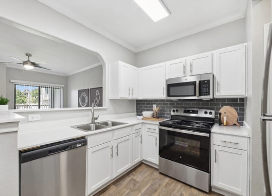 Model Kitchen with White Cabinets, Wood-Style Flooring and View of Living Room at Hidden Creek Apartments located in Lewisville, TX.