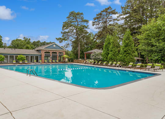 Resort-style swimming pool with lounge chairs and trees in the background
