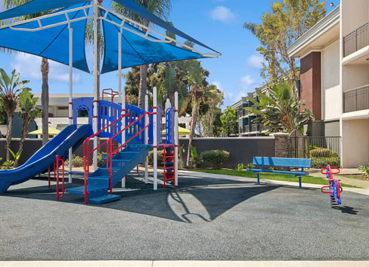 Community Playground with Slide and Blue Canopy at Madison Park Apartments located in Anaheim, CA.