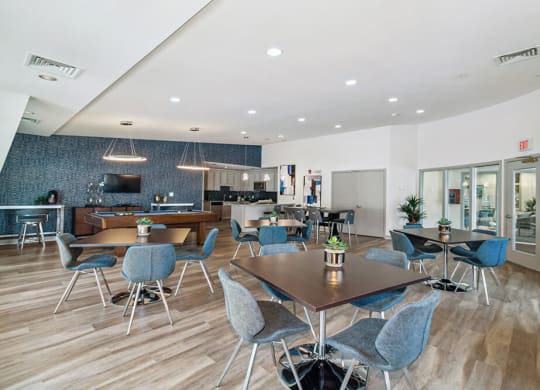 Community area with tables and chairs and a kitchen in the background
