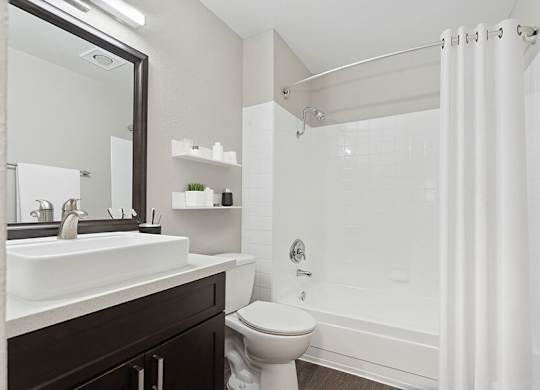 Model Bathroom with Dark Wood Cabinets, Wood-Style Flooring and Shower/Tub at Horizon Apartments located in Santa Ana, CA.
