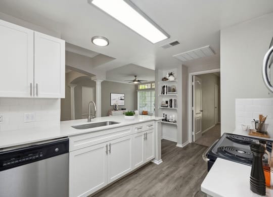 Model Kitchen with Wood-Style Flooring, White Cabinets and View of Living Room Area at Allure North Dallas Apartments located in Dallas, TX.