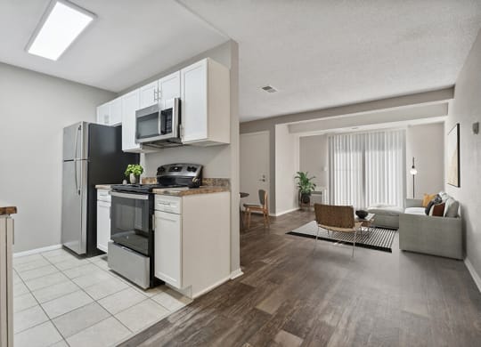 Model Kitchen with White Cabinets and Tile Flooring with View of Living Room with Wood-Style Flooring at Liberty Creek Apartments in Aurora, CO.