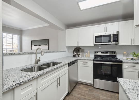 Model Kitchen with White Cabinets and Wood-Style Flooring at Chapel Hill Apartments in Lewisville, TX.