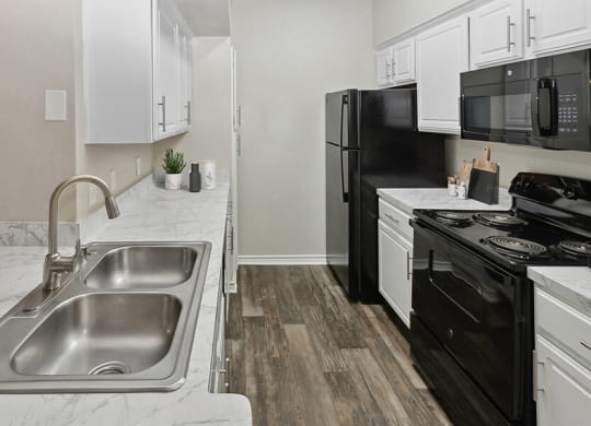 Model Kitchen with White Cabinets and Wood-Style Flooring at Belmont at Duck Creek Apartments in Garland, TX.